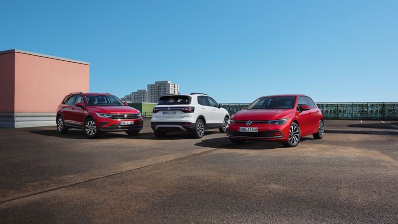 Ein roter Golf, ein weißer T-Cross und ein roter Tiguan stehen nebeneinander auf einem Parkdeck unter blauem Himmel.