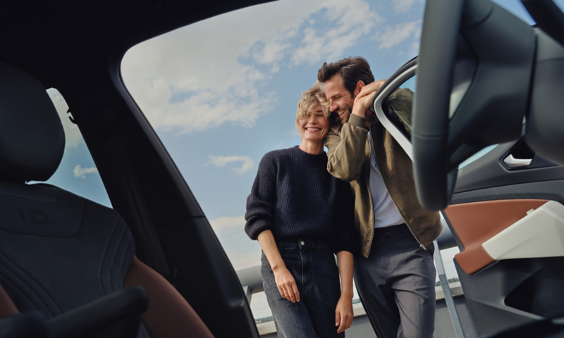 A couple leans against the open door of a car.