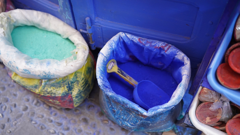 Des sacs avec des pigments de couleur bleue et verte intenses et une pelle en plastique dans les ruelles de Chefchaouen.
