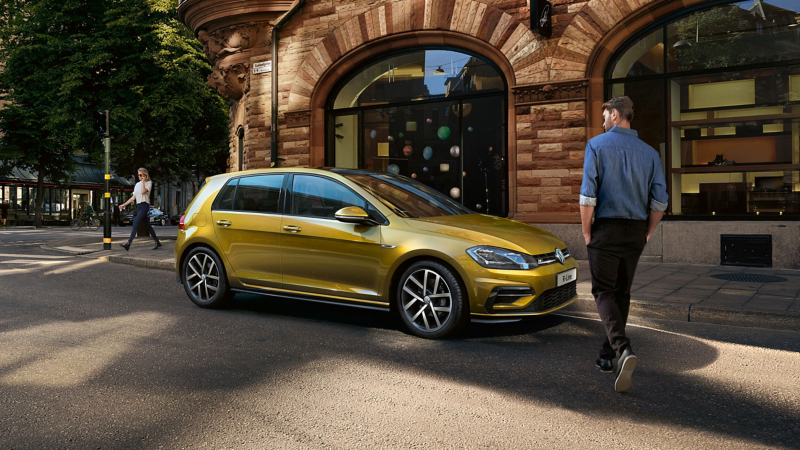 A man walking towards a yellow Volkswagen vehicle parked on a city street