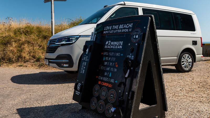 A VW California parked on a beach next to a beach clean sign. 