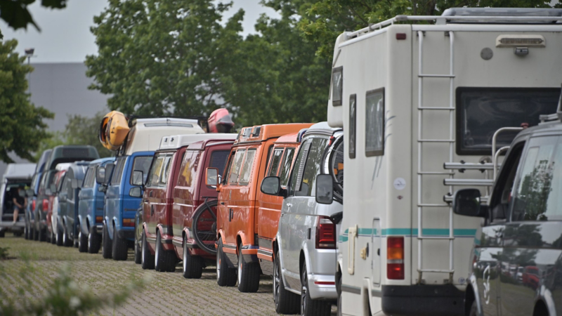 Photo showing a row of vintage VW vans driving down a road. 