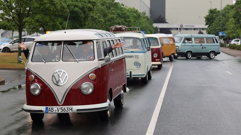 Photo showing a row of vintage VW vans driving down a road. 