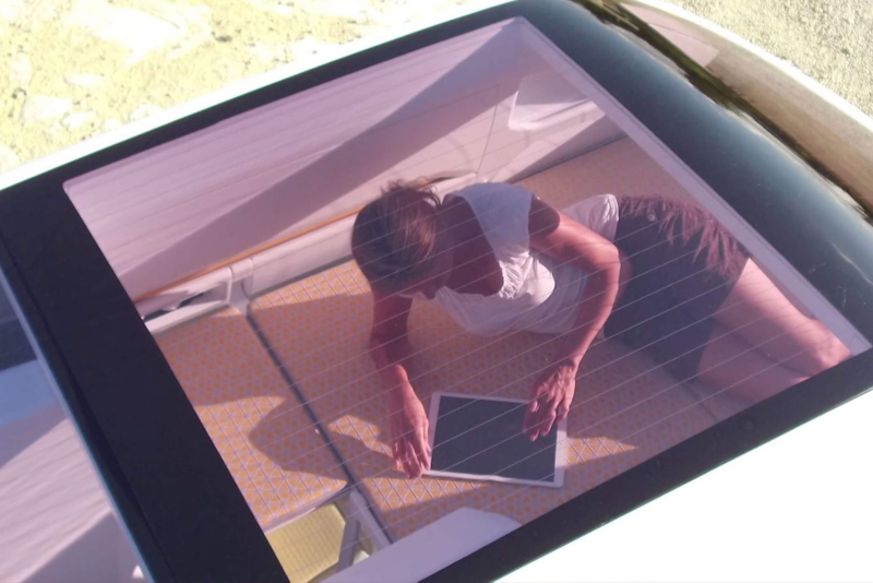Rooftop window of California XXL van. Woman lounging on bed reading tablet device.