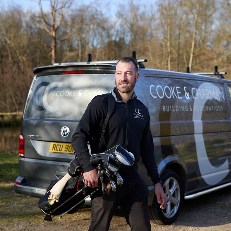 Charlie the owner of Cooke & Charman walking away from a VW van carrying golf clubs. 