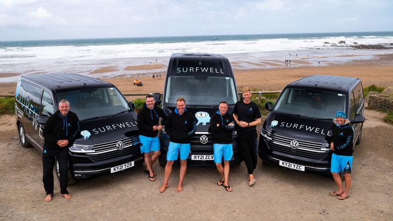 A photo of the Surfwell team standing infront of 3 Surfwell branded VW vans. 