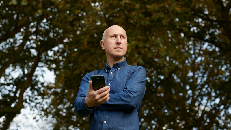 Ben Lane, co-founder of Zap-Map standing proudly in front of a tree holding a phone.