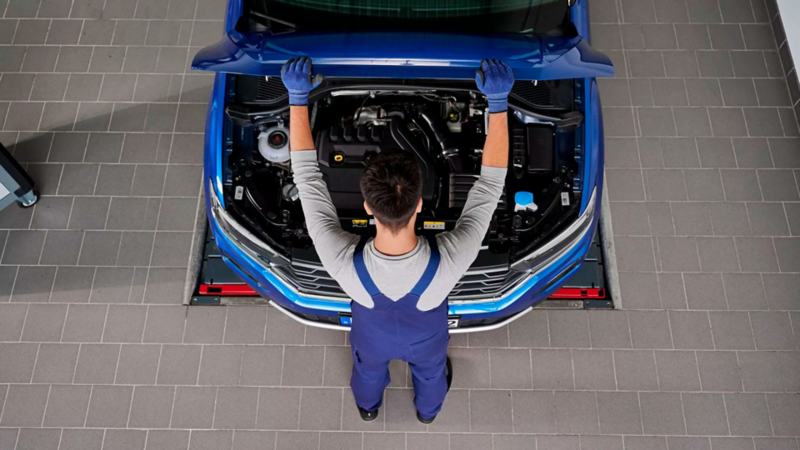 Técnico de Volkswagen abre cofre de auto para revisar el motor de un SUV de color azul. 