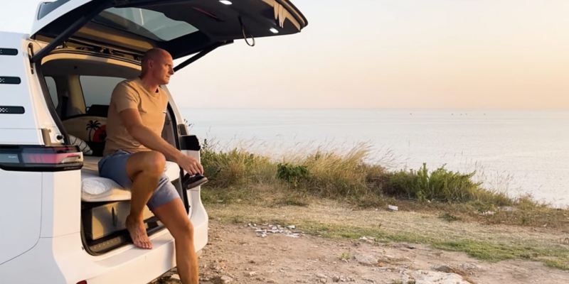 Alexander Dahlin sitter i bakluckan på en VW ID. Buzz och tittar ut över soluppgången.