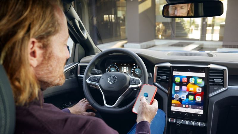 En man med telefon i handen sitter bakom ratten i nya VW Amarok och kopplar ihop sig med infotainmentsystemet