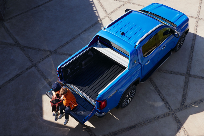 An Amarok from above, with two people sitting on the tailgate.