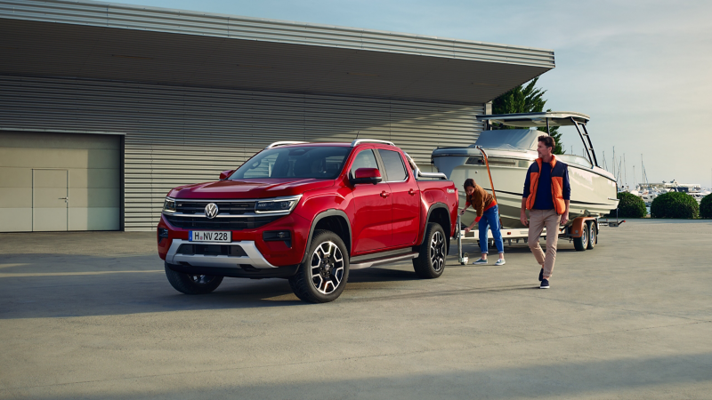 VW Amarok Style mit angekoppeltem Hänger, auf dem ein Boot geladen ist.