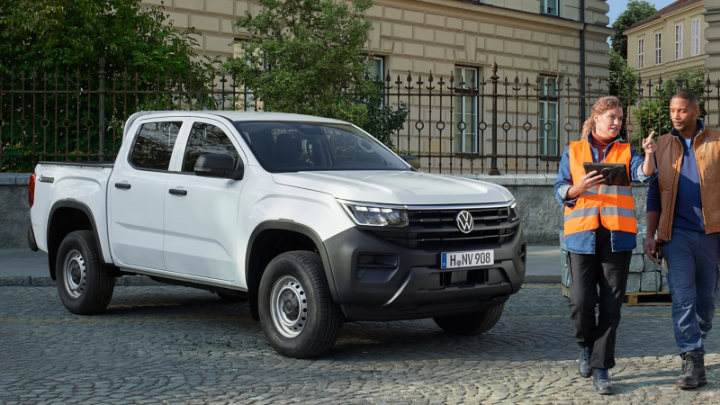 Ein VW Amarok steht vor einem Gebäude, zwei Arbeiter gehen neben dem Fahrzeug her
