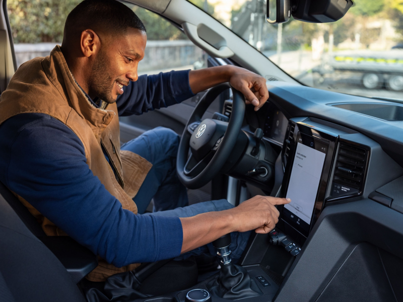 En man sitter i förarsätet på en VW Amarok med fingret på infotainmentsystemets skärm.