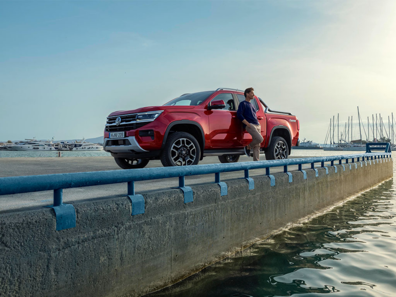VW Amarok Style parkt auf einem Pier. Ein Mann lehnt lässig an dem Fahrzeug.