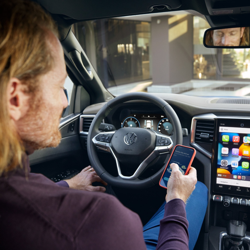 En man sitter i förarplatsen på en VW Amarok med en mobiltelefon i handen
