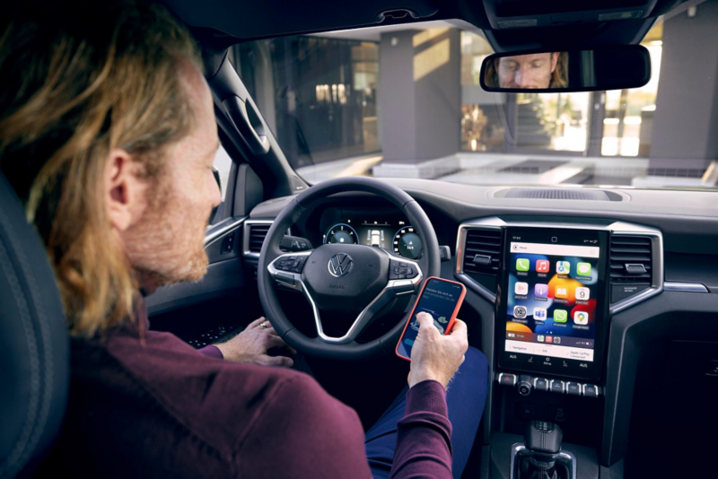 Una mujer usando el teléfono móvil y la pantalla de su vehículo VW.