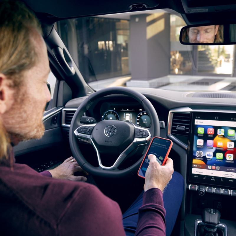Person hinter dem Steuer eines Volkswagen mit einem Smartphone in der Hand.