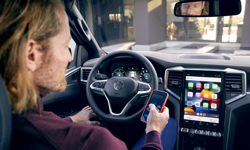 Ein Mann sitzt am Steuer seines parkenden VW Amarok und blickt in sein Smartphone.