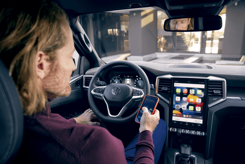 Mężczyzna ze smartfonem za kierownicą Volkswagena Amaroka.