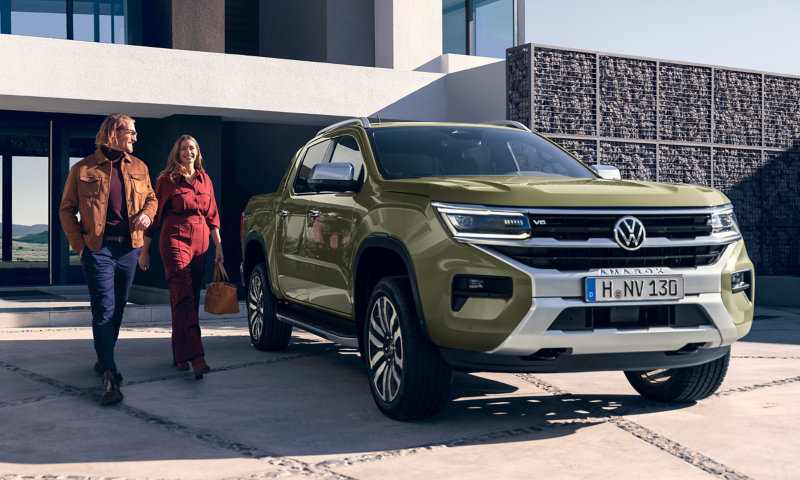 Ein VW Amarok ist vor einem modernen Haus geparkt und zwei Leute laufen darauf zu.