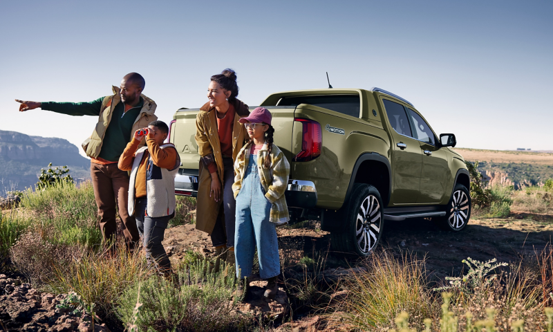 Eine Familie steht vor einem VW Amarok auf einer Wiese.