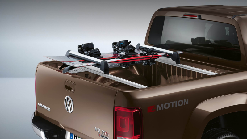 Une vue arrière d'un pick-up Volkswagen Amarok marron, dont la benne est équipée d'un porte-skis transportant des skis.