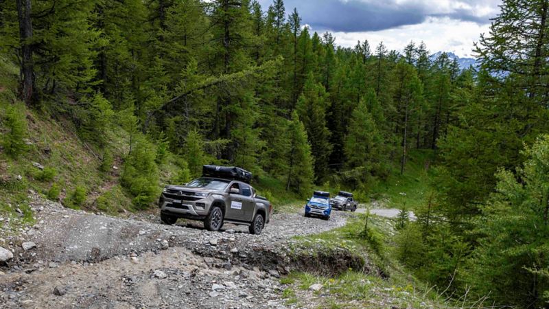 Trois amaroks qui se déplacent sur une route rocailleuse et boisée en terrain montagneux