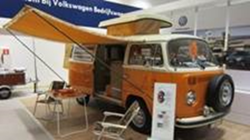 Een oranje Volkswagen camper staat binnen met de deuren open