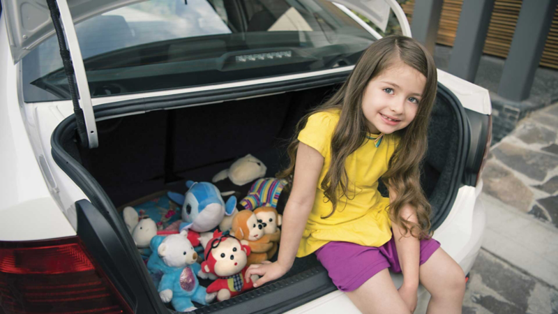 Niña sentada en cajuela de Vento Startline 2022 con peluches a su lado. 