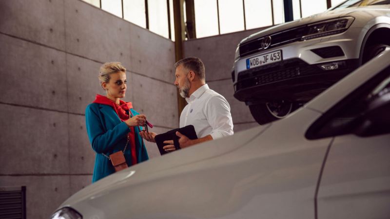 Un technicien Volkswagen et une femme discutent au milieu des véhicules présents dans l'atelier.