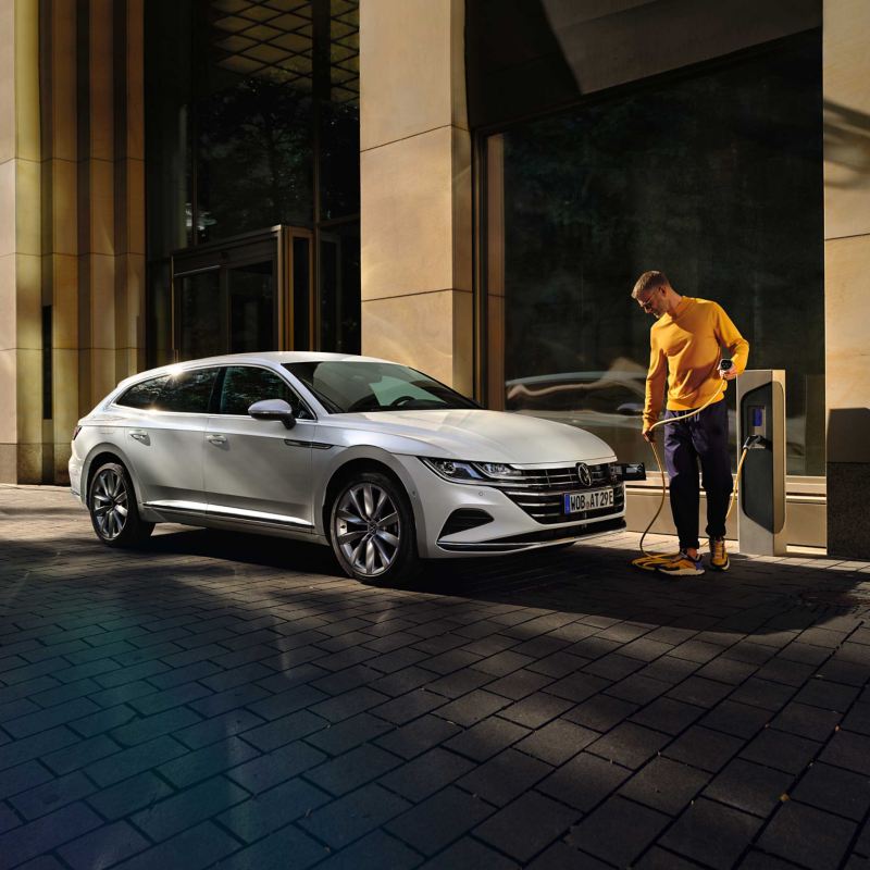 A man holding a charging cable to plug into a VW Arteon e-hybrid car