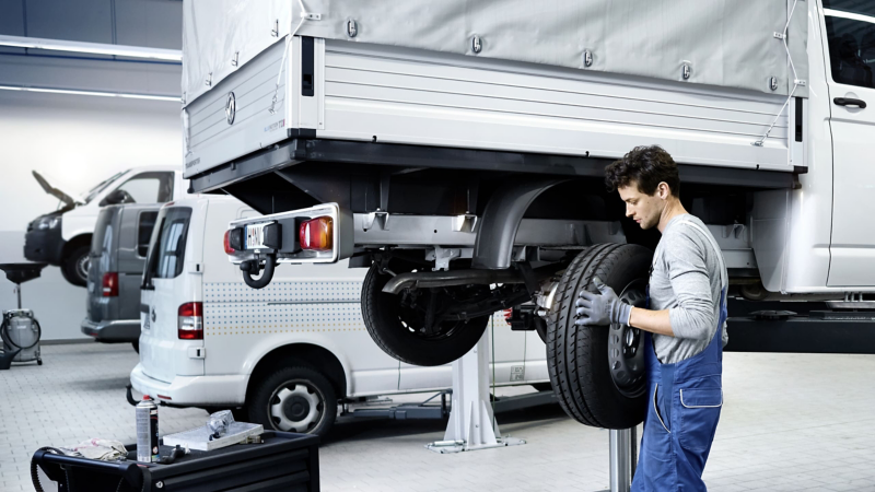 Pracownik serwisu zmienia koło w dostawczym Volkswagenie.