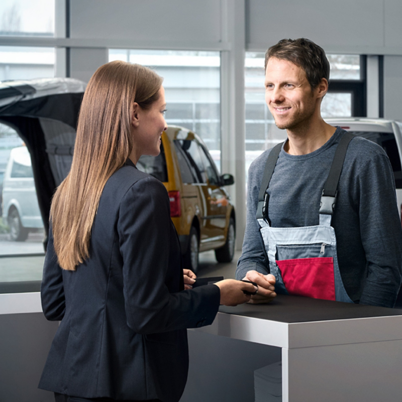 Ein Mann spricht mit einer Frau in einem Autohaus über einen Tresen hinweg.