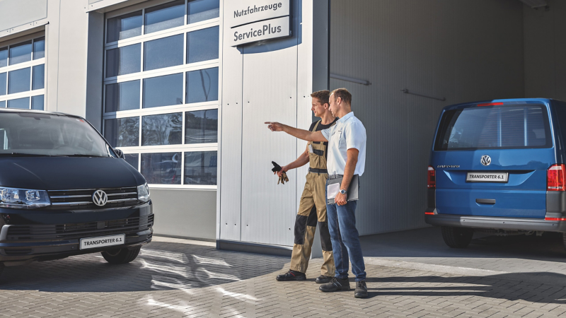 Dwóch pracowników serwisu rozmawia przed wjazdem do warsztatu.