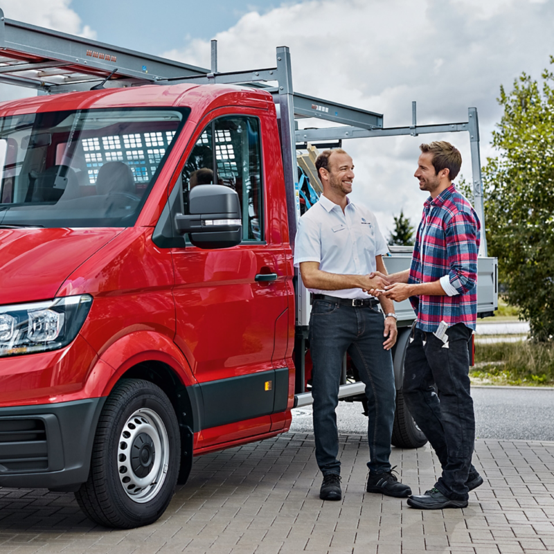 Ein Handwerker und ein VW Partner stehen neben einem VW Crafter Pritschenwagen mit Umbau.