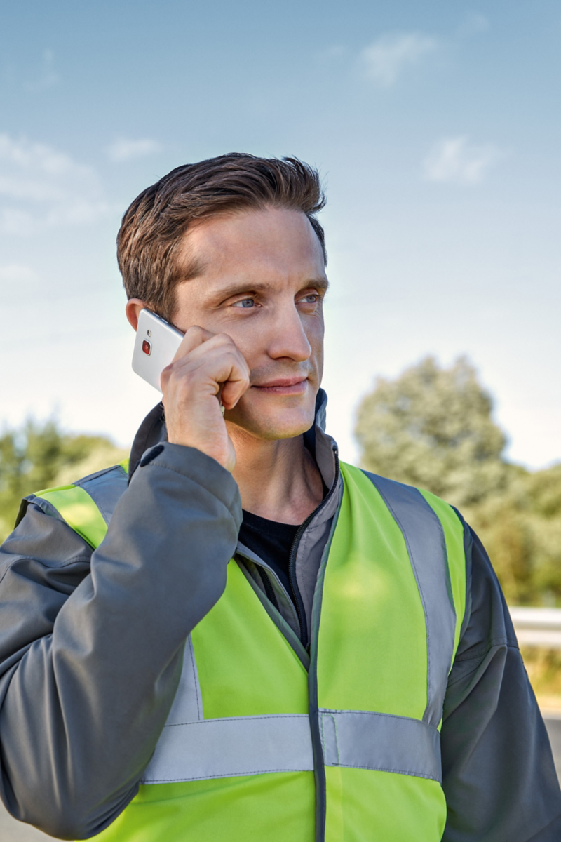 Ein Mann mit Warnweste telefoniert mit einem Smartphone.