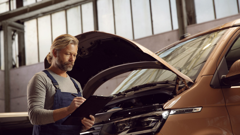 Un addetto VW in officina, di fronte a un veicolo Volkswagen, scrive su un blocco.