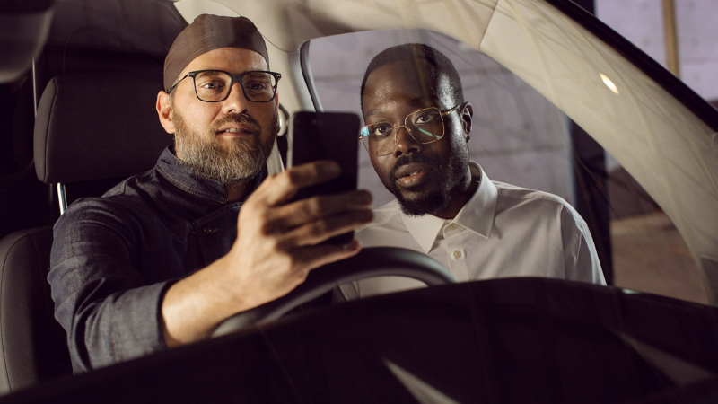 Un homme est assis sur le siège du conducteur VW, un autre homme à côté de lui. Les deux regardent un téléphone portable.