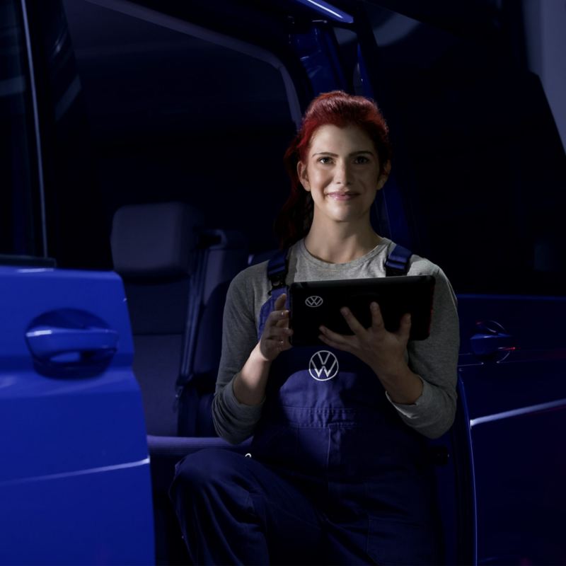 Eine Mechanikerin mit Tablet in der Hand lehnt an einem Volkswagen Nutzfahrzeug.
