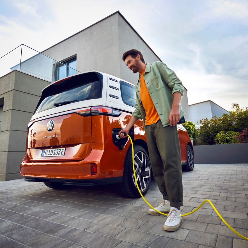 En man pluggar i laddkontakten i en VW ID. Buzz elminibuss.