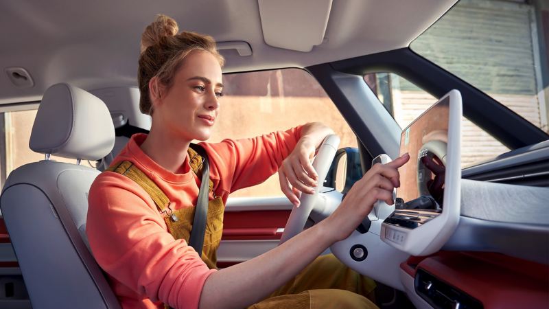 Eine Frau sitzt auf dem Fahrersitz eines ID. Buzz und bedient das Digital Cockpit.