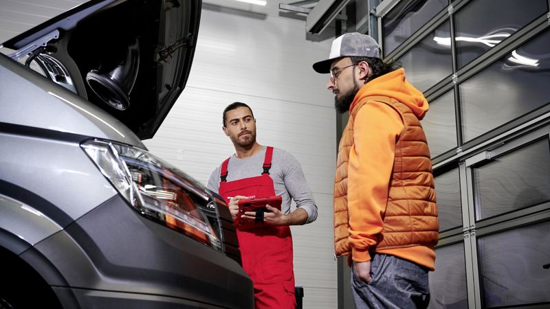 Ein Servicemitarbeiter und ein Mann stehen bei einem Volkswagen Fahrzeug.