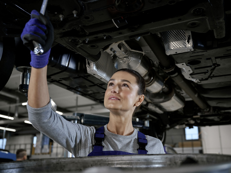 Eine Mechanikerin schraubt am Unterboden eines VW Nutzfahrzeugs.