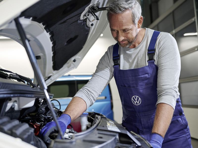 Ein Servicemitarbeiter begutachtet den Motorraum eines Volkswagen Fahrzeugs.