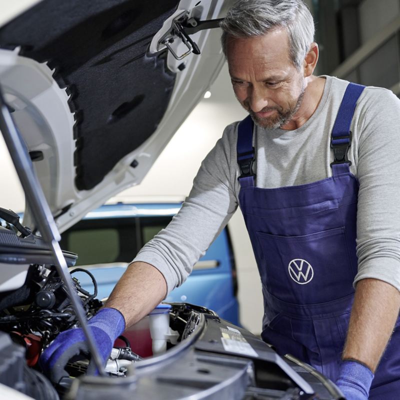 Ein Servicemitarbeiter begutachtet den Motorraum eines Volkswagen Fahrzeugs.