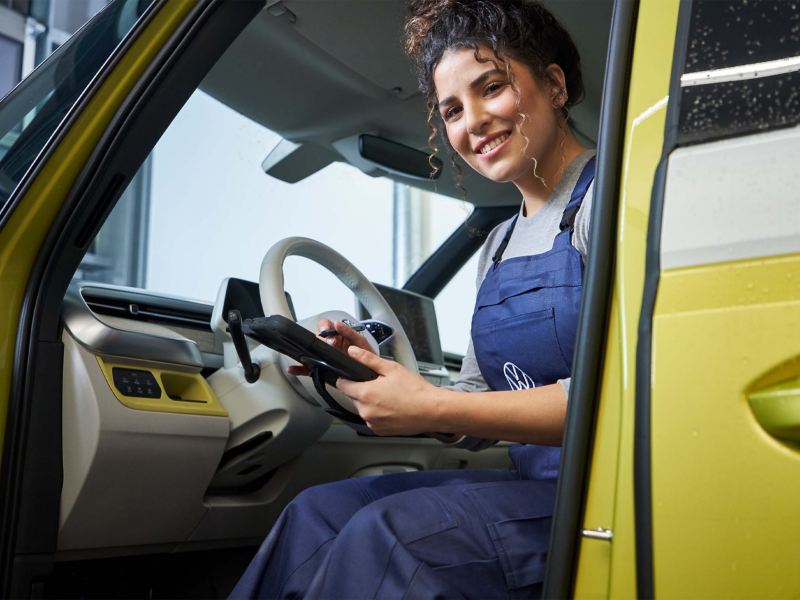 Eine Mechanikerin sitzt bei geöffneter Tür mit einem Tablet in der Hand in einem Volkswagen ID. Buzz.