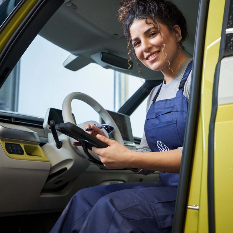 Eine Mechanikerin sitzt bei geöffneter Tür mit einem Tablet in der Hand in einem Volkswagen ID. Buzz.