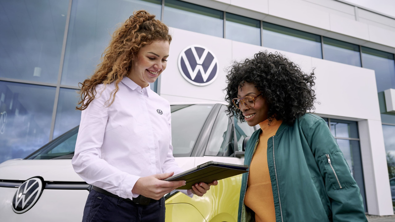 Ein Mann mit Tablet unterhält sich mit einer im einem VW sitzenden Frau vor einem Volkswagen Nutzfahrzeuge Service Center.