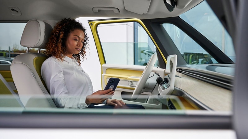 Eine Frau blickt auf dem Fahrersitz eines Fahrzeugs auf ihr Smartphone